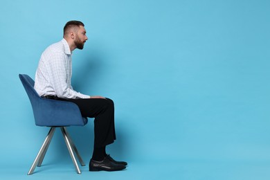 Man with poor posture sitting on chair against light blue background, space for text