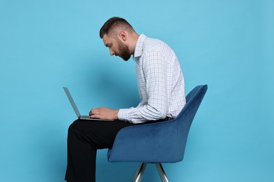 Man with poor posture sitting on chair and using laptop against light blue background