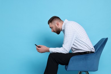 Man with poor posture sitting on chair and using smartphone against light blue background, space for text