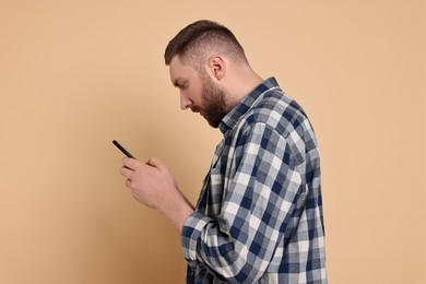 Photo of Man with poor posture using smartphone on pale orange background
