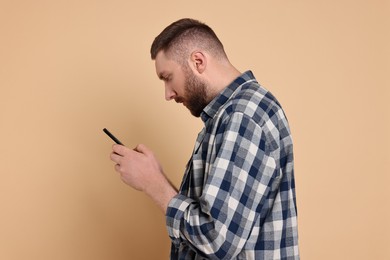 Man with poor posture using smartphone on pale orange background