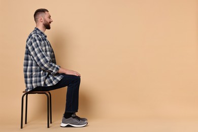 Man with good posture sitting on chair against pale orange background, space for text