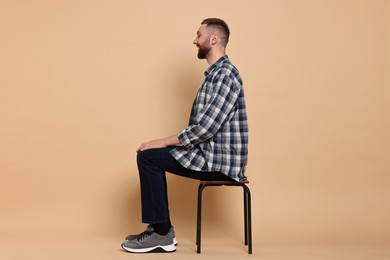 Man with good posture sitting on chair against pale orange background