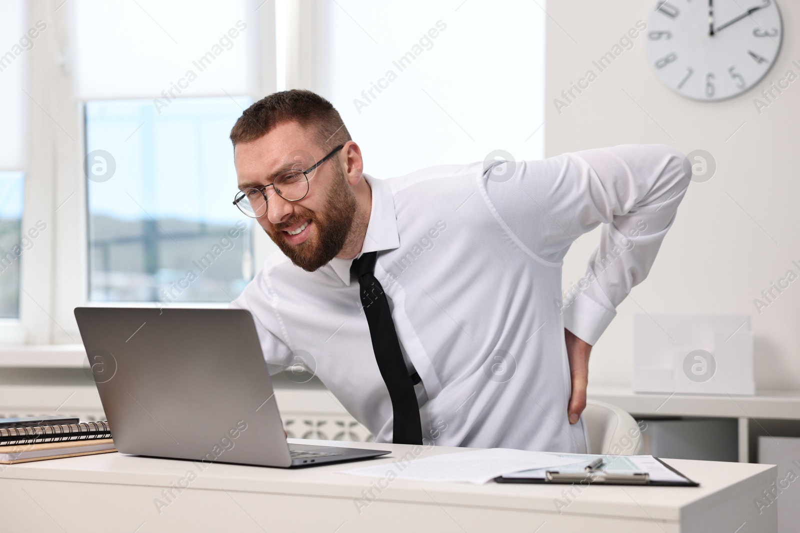 Photo of Man suffering from back pain in office. Symptom of poor posture