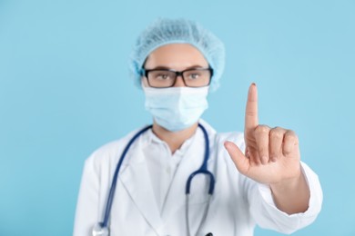 Doctor pointing at something on light blue background, selective focus