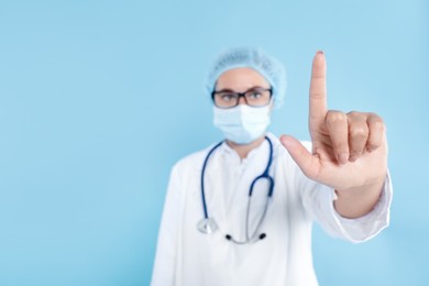 Photo of Doctor pointing at something on light blue background, selective focus. Space for text