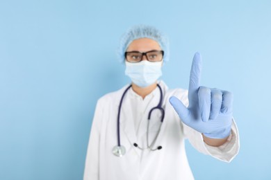 Doctor pointing at something on light blue background, selective focus