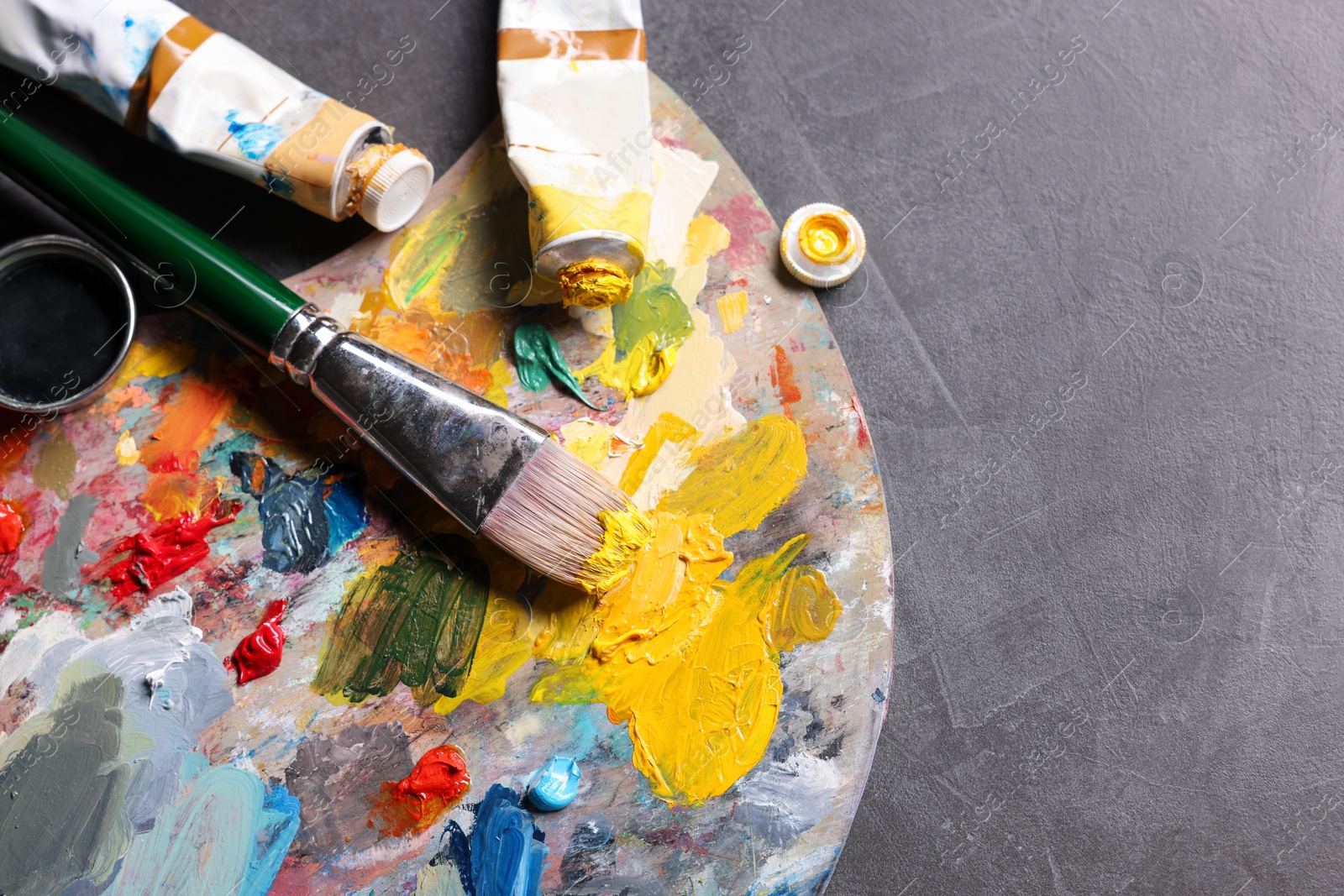 Photo of Artist's palette, brush and paints on grey table, flat lay. Space for text