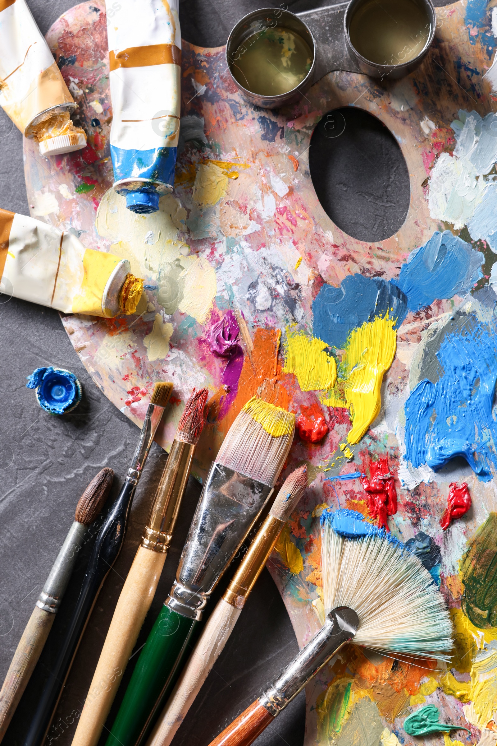 Photo of Artist's palette, brushes and paints on grey table, flat lay