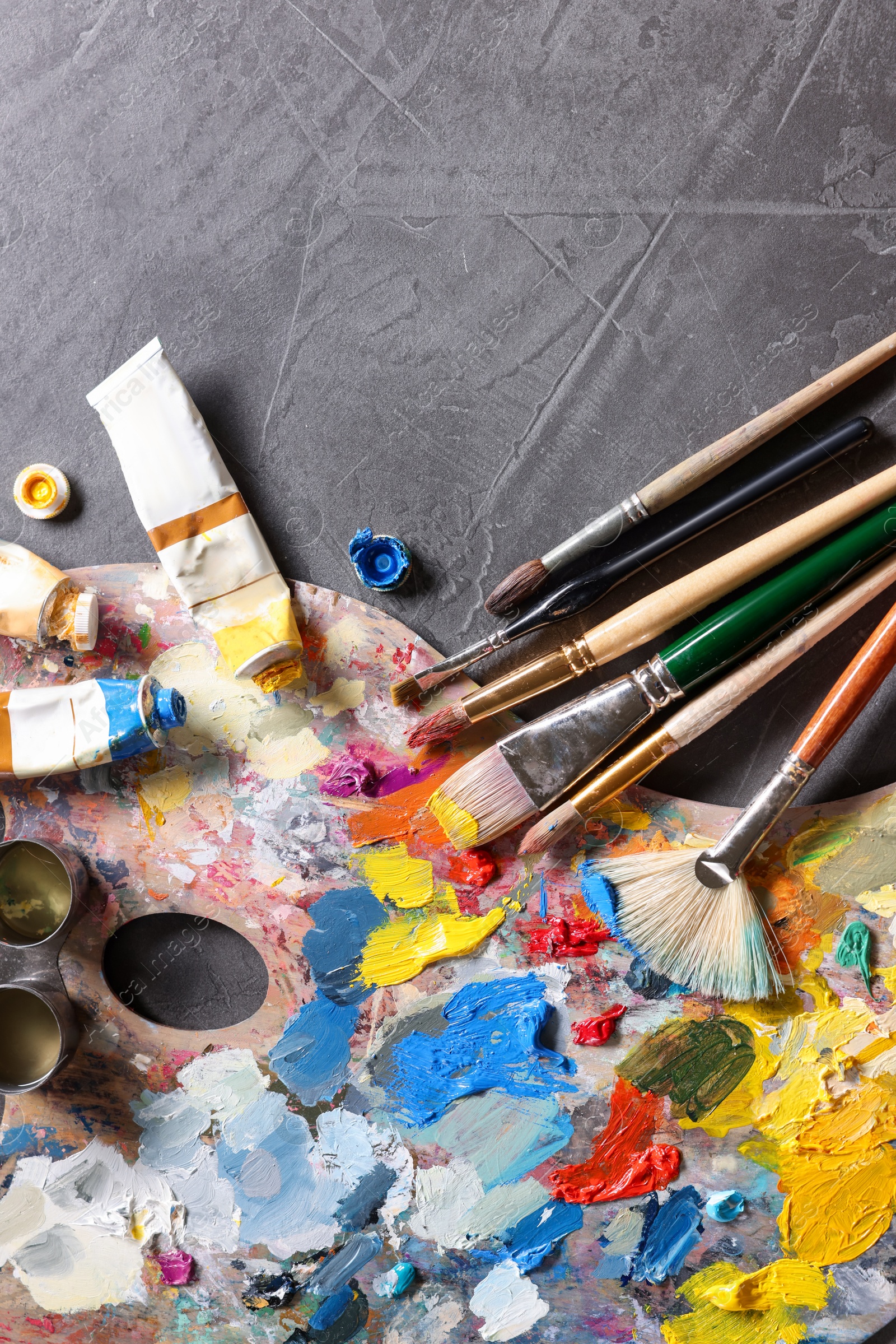 Photo of Artist's palette, brushes and paints on grey table, flat lay. Space for text