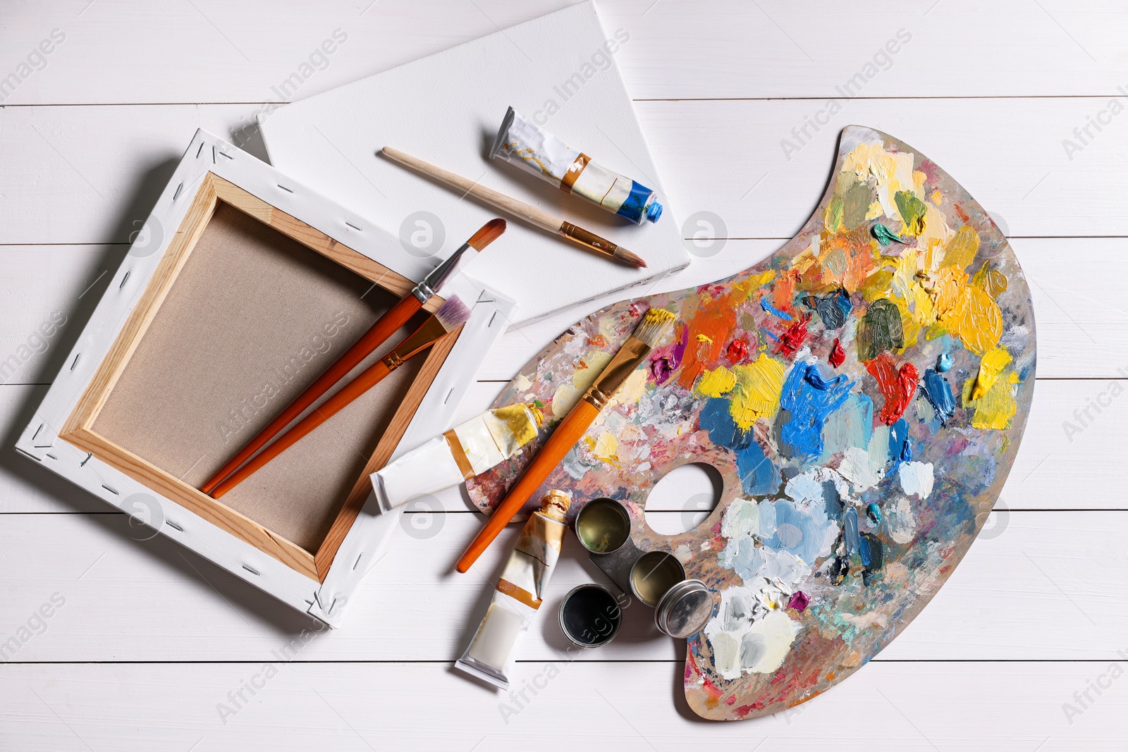 Photo of Artist's palette, brushes, paints and blank canvases on white wooden table, flat lay