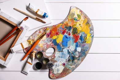 Photo of Artist's palette, brushes, paints and blank canvases on white wooden table, flat lay