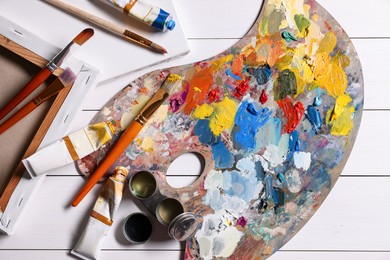 Photo of Artist's palette, brushes, paints and blank canvases on white wooden table, flat lay