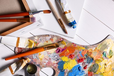 Photo of Artist's palette, brushes, paints and blank canvases on white wooden table, flat lay