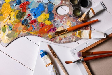 Photo of Artist's palette, brushes, paints and blank canvases on white wooden table, flat lay