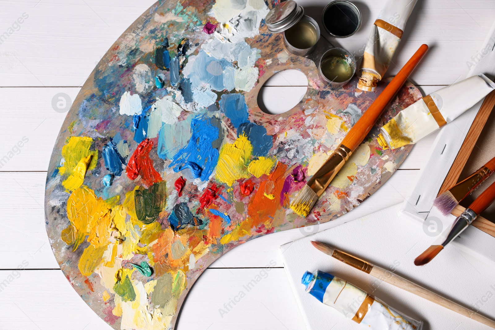 Photo of Artist's palette, brushes, paints and blank canvases on white wooden table, flat lay