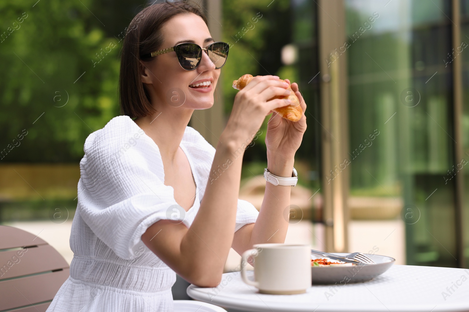 Photo of Happy woman having tasty breakfast in outdoor cafe