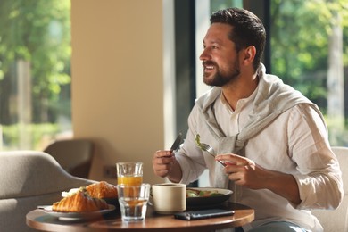 Photo of Happy man having tasty breakfast in cafe, space for text
