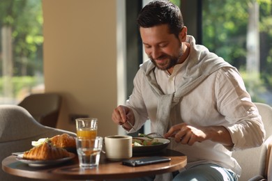 Happy man having tasty breakfast in cafe, space for text