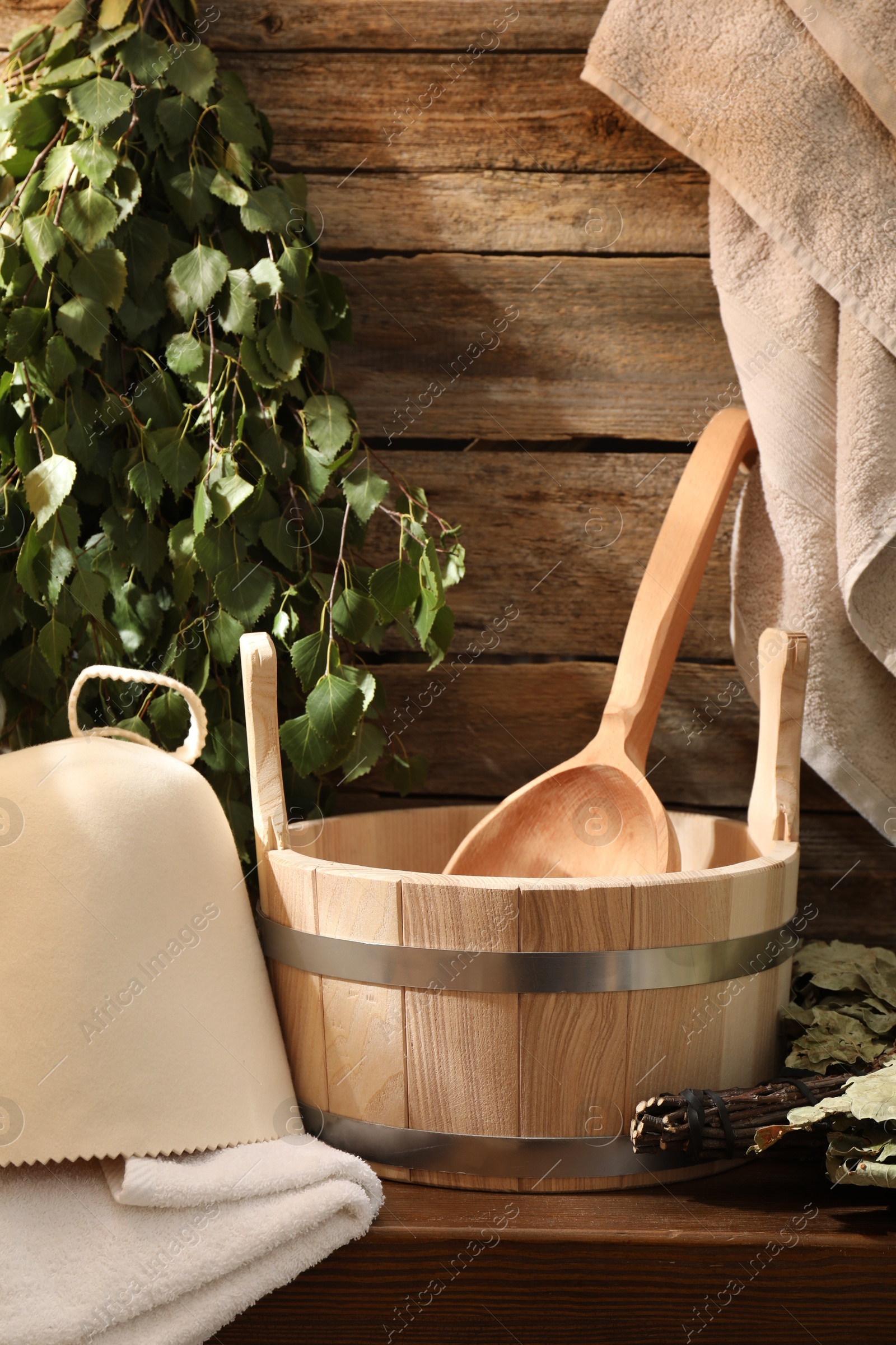 Photo of Sauna equipment. Bucket with ladle, felt wool hat, towels and whisks on wooden table indoors