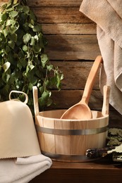 Photo of Sauna equipment. Bucket with ladle, felt wool hat, towels and whisks on wooden table indoors