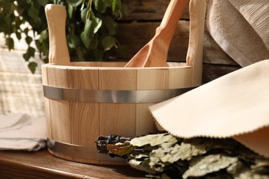 Sauna equipment. Bucket with ladle, felt wool hat and oak whisk on wooden table indoors, closeup