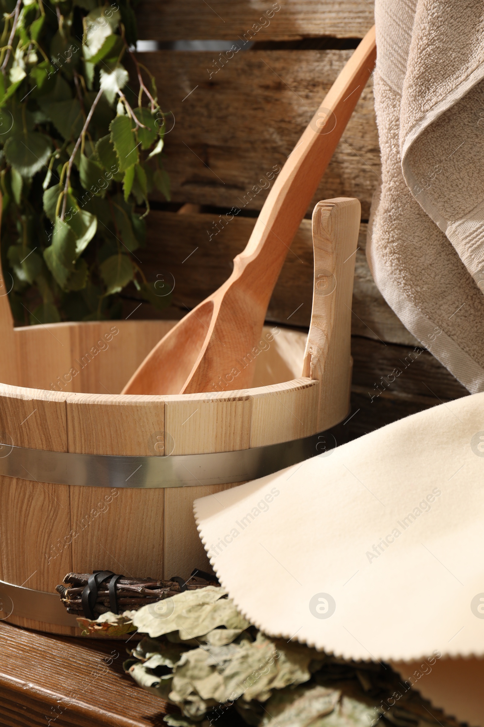 Photo of Sauna equipment. Bucket with ladle, felt wool hat and oak whisk on wooden table indoors