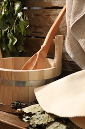 Photo of Sauna equipment. Bucket with ladle, felt wool hat and oak whisk on wooden table indoors