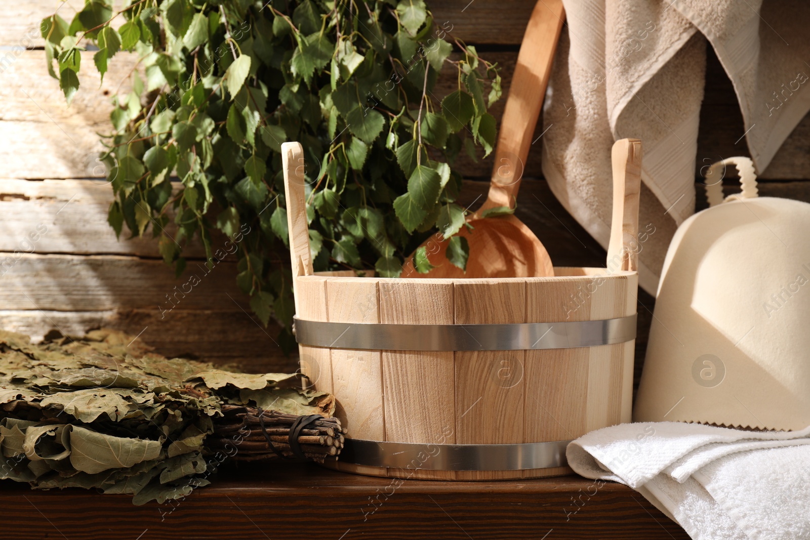 Photo of Sauna equipment. Bucket with ladle, felt wool hat, whisks and towels on wooden table indoors