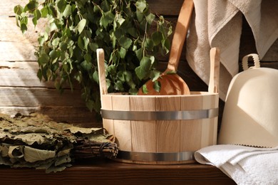 Sauna equipment. Bucket with ladle, felt wool hat, whisks and towels on wooden table indoors