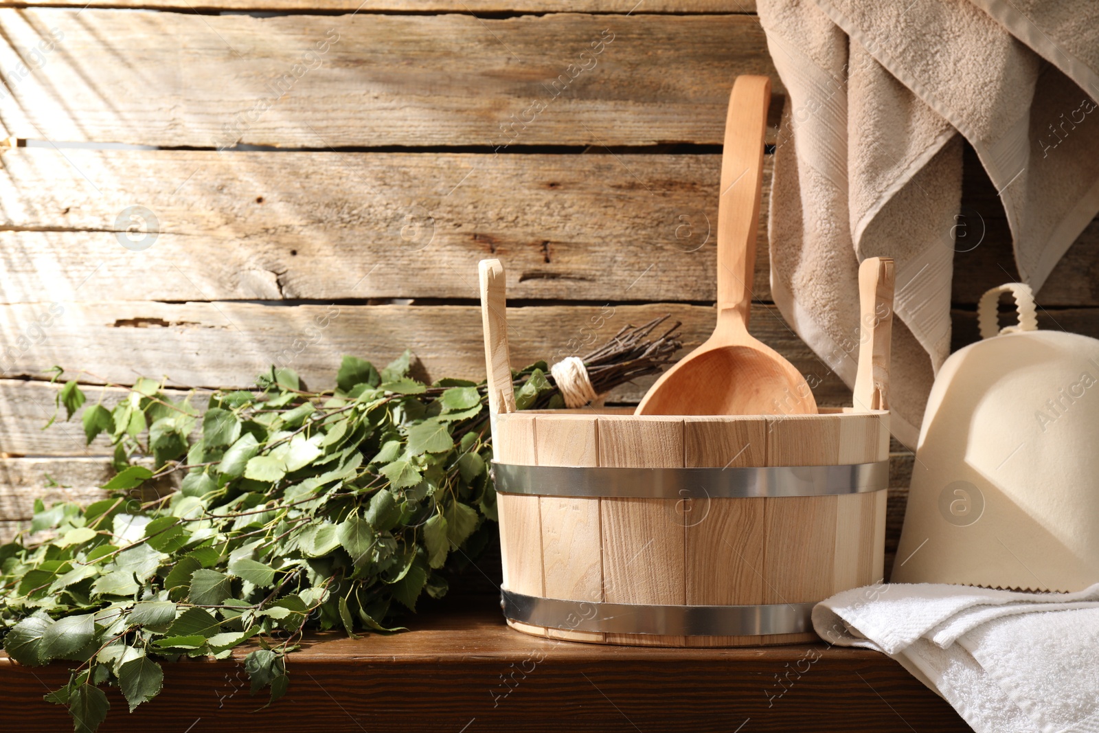 Photo of Sauna equipment. Bucket with ladle, felt wool hat, birch whisk and towels on wooden table indoors