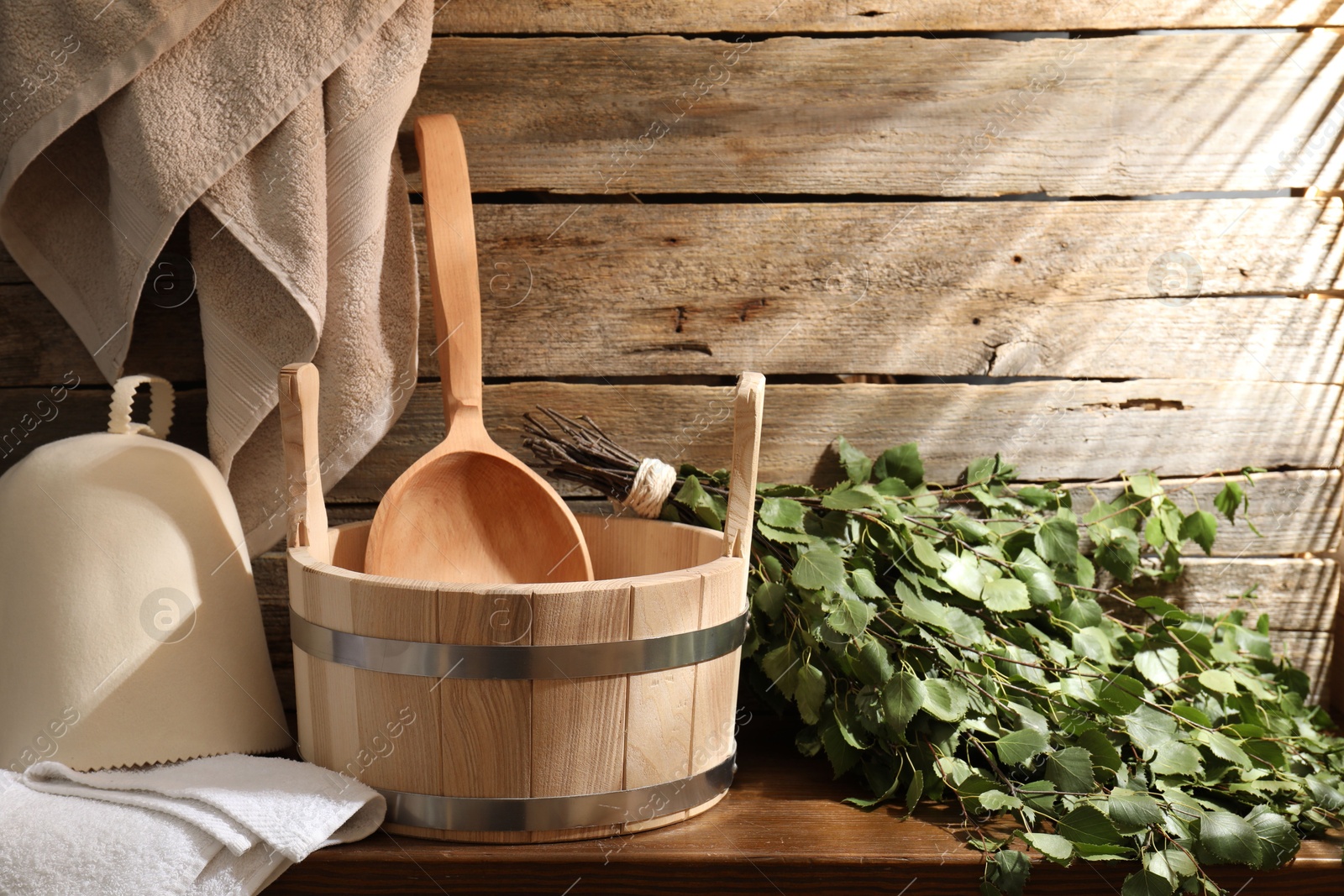 Photo of Sauna equipment. Bucket with ladle, felt wool hat, birch whisk and towels on wooden table indoors