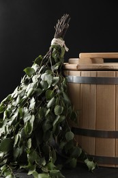 Photo of Sauna equipment. Bucket and birch whisk on black textured surface, closeup