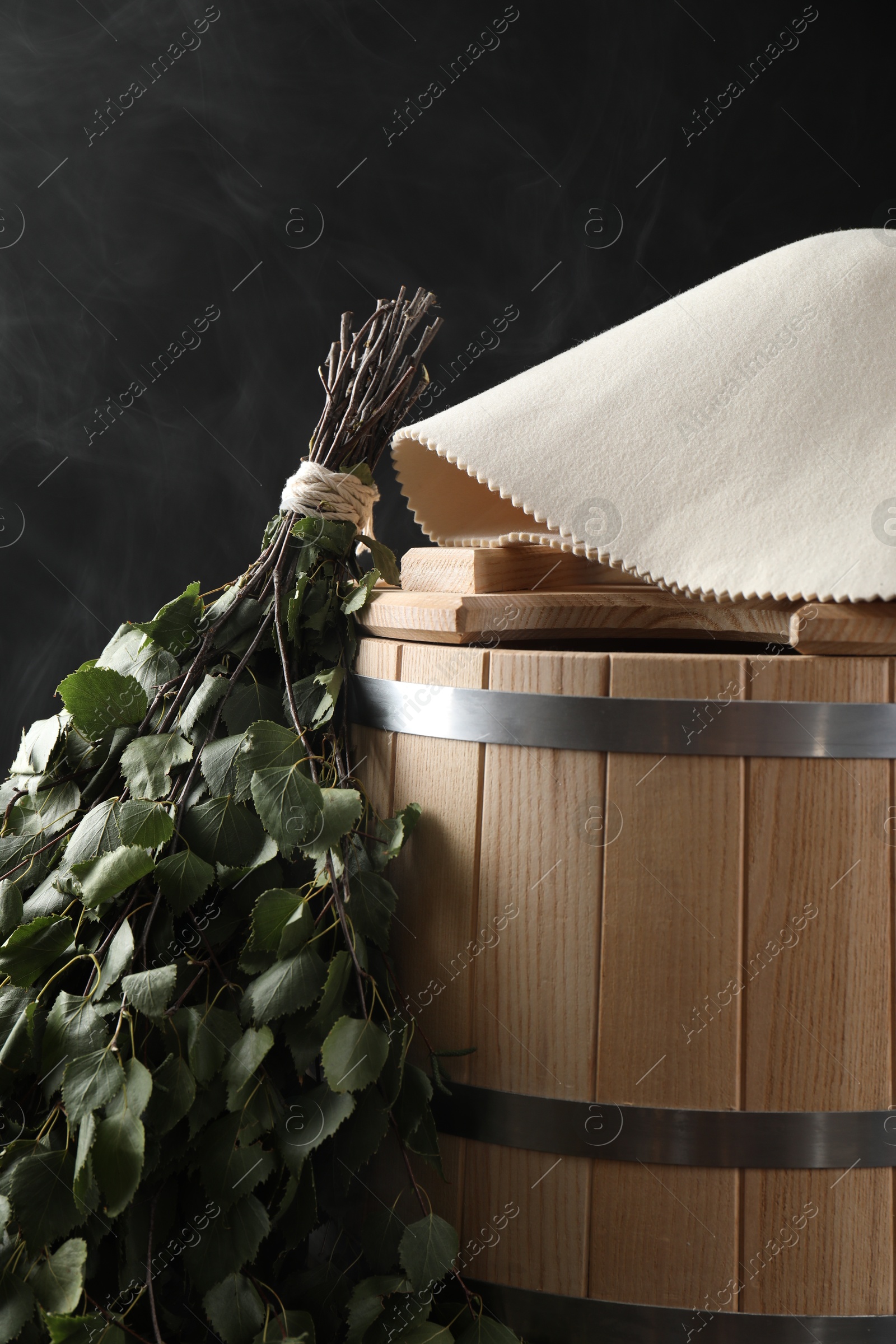 Photo of Sauna equipment. Bucket, birch whisk and felt wool hat on black background, closeup