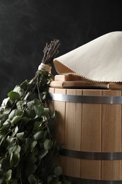 Photo of Sauna equipment. Bucket, birch whisk and felt wool hat on black background, closeup