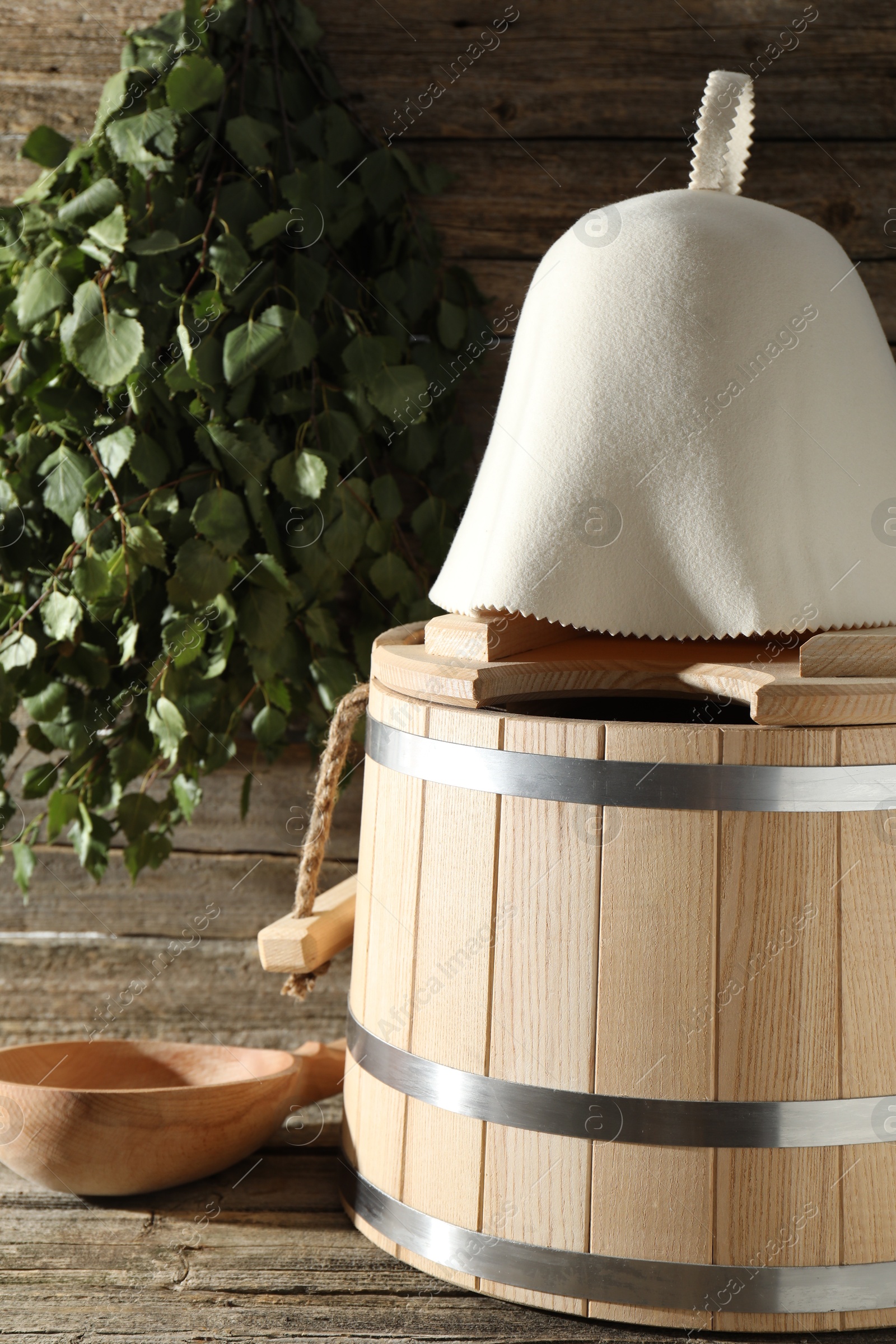 Photo of Sauna equipment. Bucket, felt wool hat and ladle on wooden surface