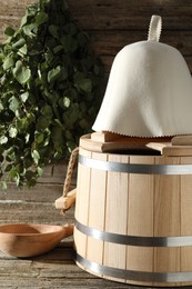 Photo of Sauna equipment. Bucket, felt wool hat and ladle on wooden surface