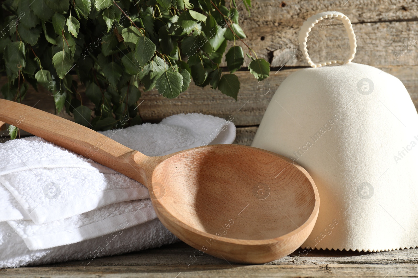 Photo of Sauna equipment. Felt wool hat, ladle and towel on wooden surface, closeup