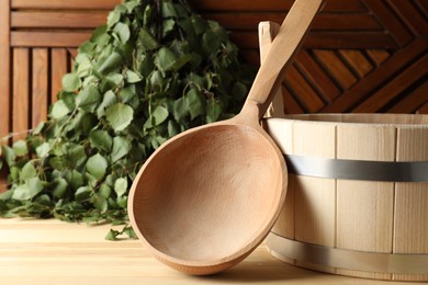 Photo of Sauna equipment. Bucket, ladle and birch whisk on wooden surface, closeup