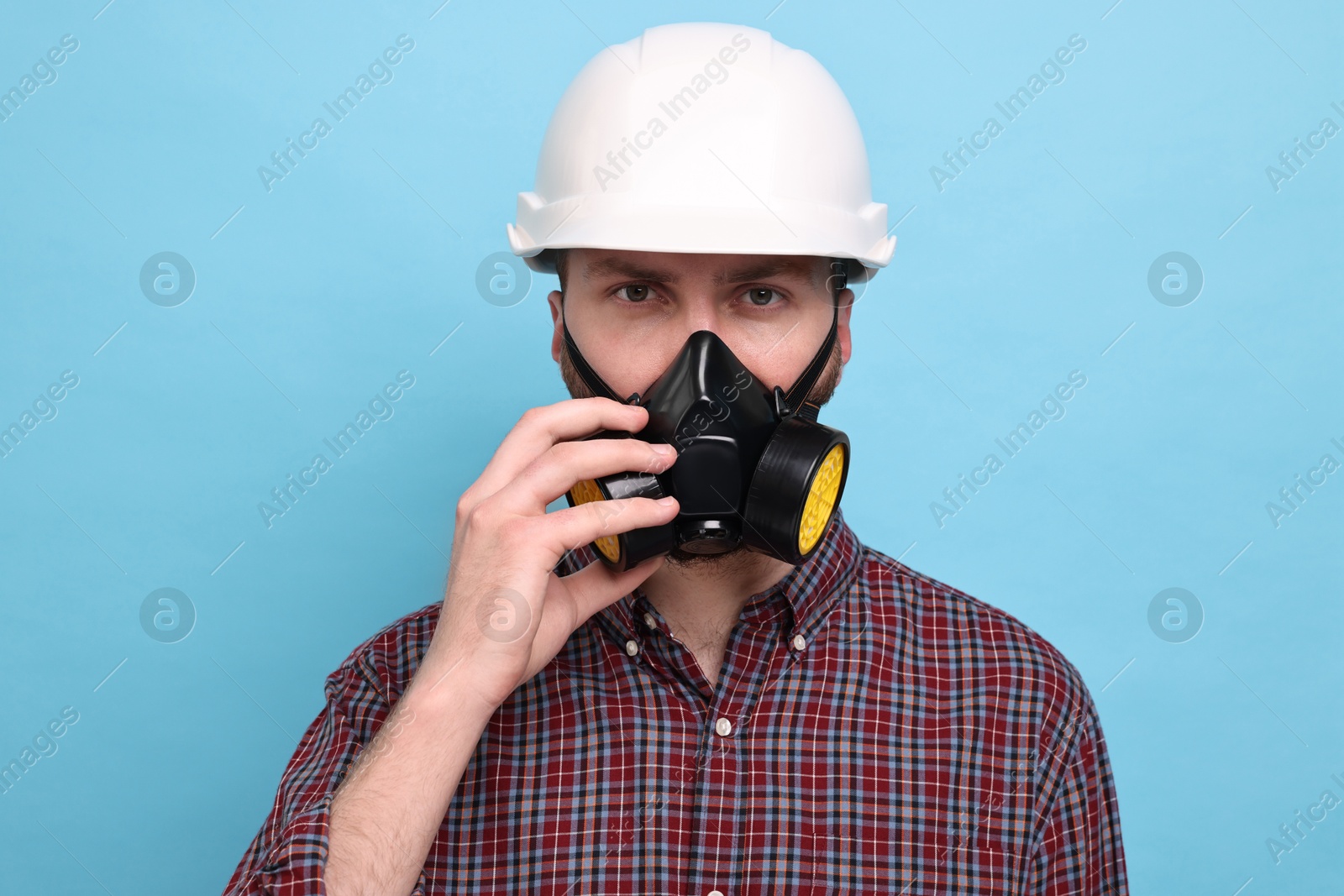 Photo of Man in respirator mask and hard hat on light blue background