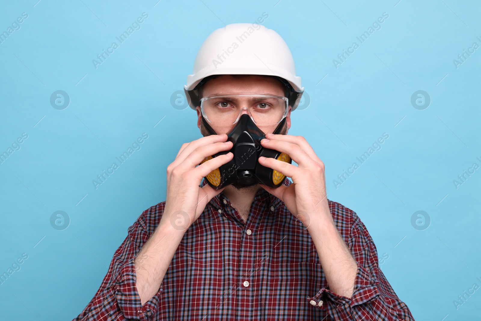 Photo of Man in respirator mask and hard hat on light blue background