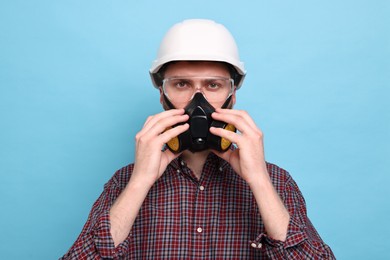 Photo of Man in respirator mask and hard hat on light blue background