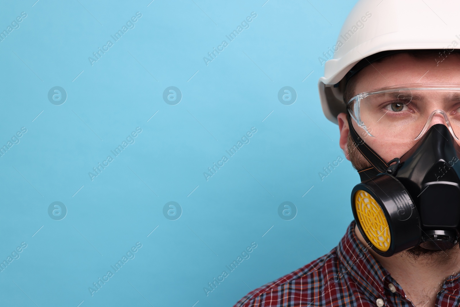 Photo of Man in respirator mask and hard hat on light blue background. Space for text