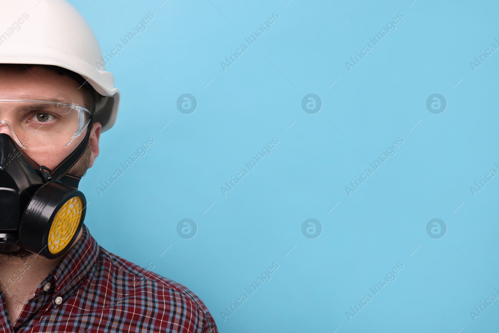 Photo of Man in respirator mask and hard hat on light blue background. Space for text