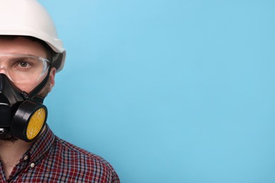 Man in respirator mask and hard hat on light blue background. Space for text