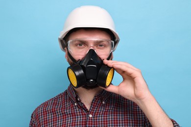 Man in respirator mask and hard hat on light blue background