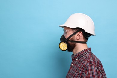 Man in respirator mask and hard hat on light blue background. Space for text