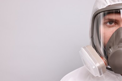 Man wearing protective suit with respirator mask on light background. Space for text