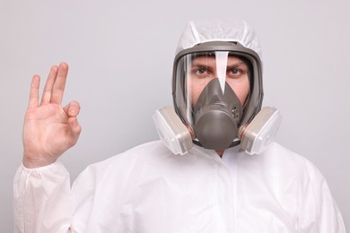 Photo of Man wearing protective suit with respirator mask showing OK gesture on light background