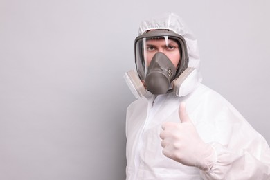 Photo of Man wearing protective suit with respirator mask showing thumb up on light background. Space for text
